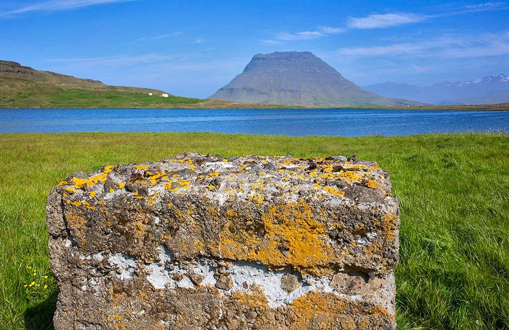 A lichen-covered concrete block on the point, with the lagoon, the farm Lárkot and the mountain Kirkjufell beyond.